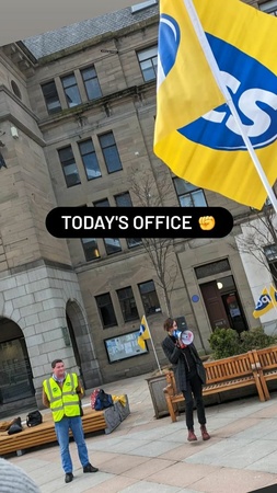 Image shows picket with megaphone and flag with the message "TODAY'S OFFICE"